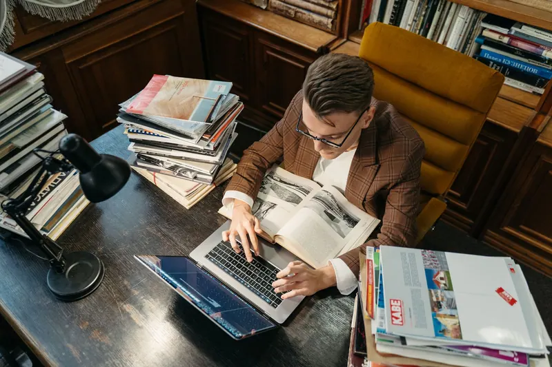 Studierender arbeitet mit Laptop und Fachliteratur in der Bibliothek
